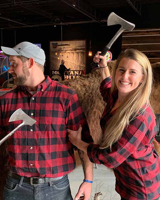 Man and woman wearing matching red flannels and holding axes.