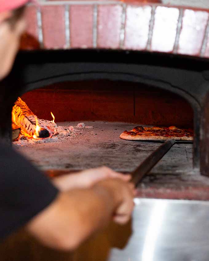 Man grabbing pepperoni pizza from an oven. Montana Nights event space. Montana Nights Top Axe-Bar + Entertainment Center in CT