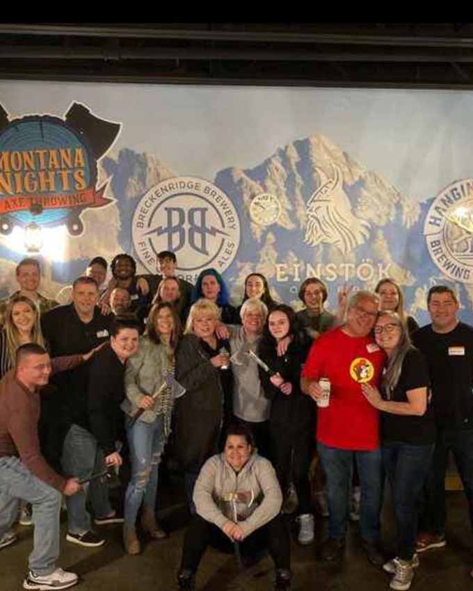Group of people holding axes and drinks posing for a group photo. Montana Nights event space. Montana Nights Top Axe-Bar + Entertainment Center in CT