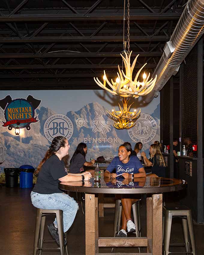 Group of women sitting at a high table and talking with drinks. Montana Nights event space. Montana Nights Top Axe-Bar + Entertainment Center in CT