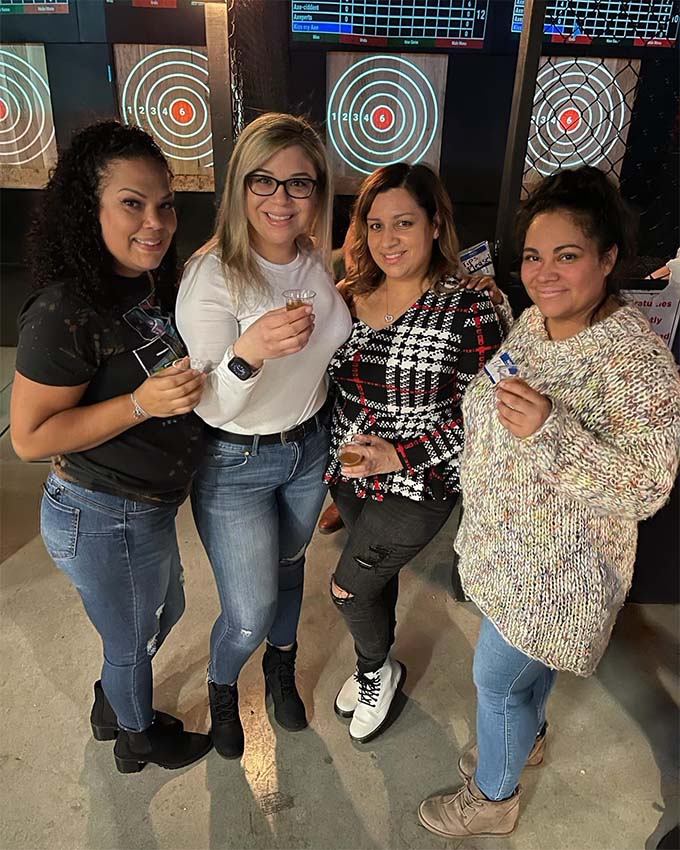 Group of four women posing for photo and holding drinks at Axe throwing venue. Montana Nights Top Axe-Bar + Entertainment Center in CT