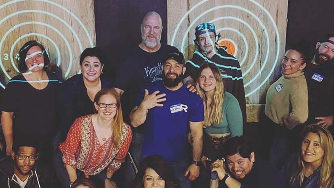 Group of adults posing and smiling in front of axe throwing targets.