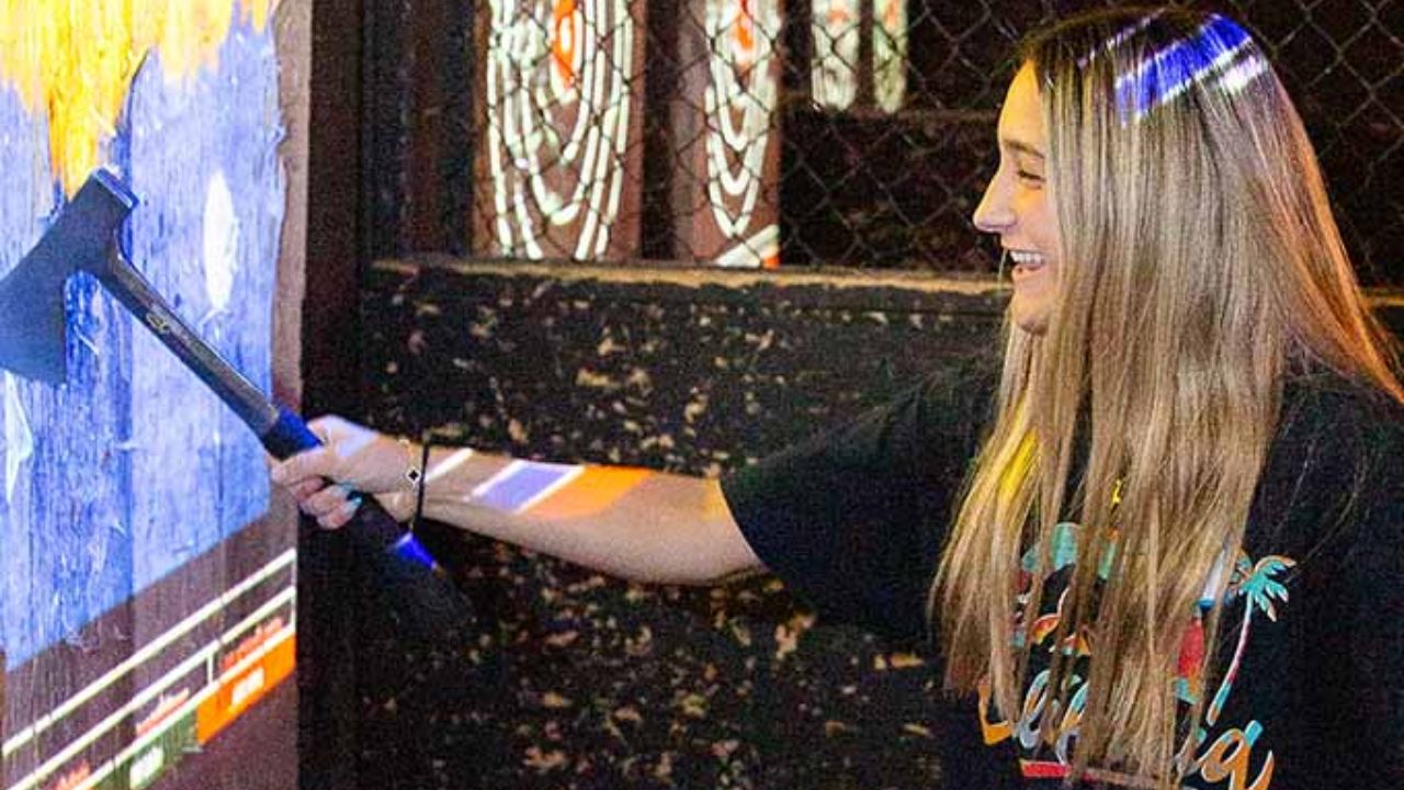 A woman holding an axe after hitting a projected axe throwing target.
