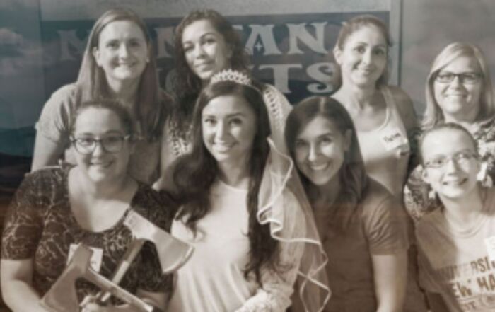 A group of women smiling and posing together, holding a sign that conveys a message or event. 