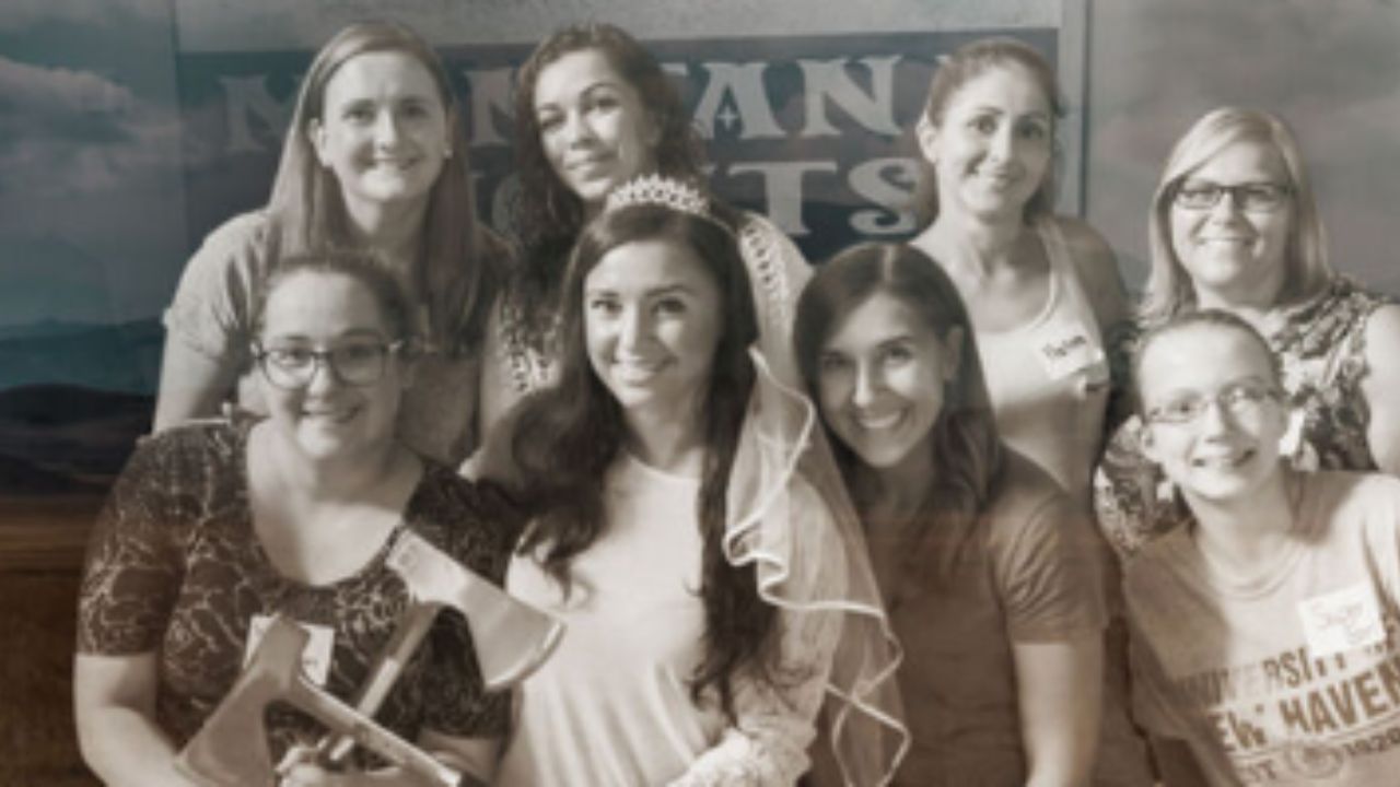 A group of women smiling and posing together, holding a sign that conveys a message or event.