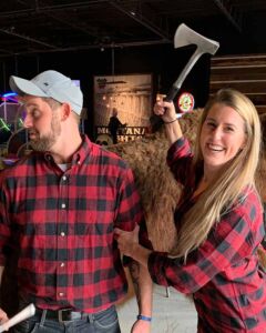 Woman smiling while holding an axe playfully with a man.