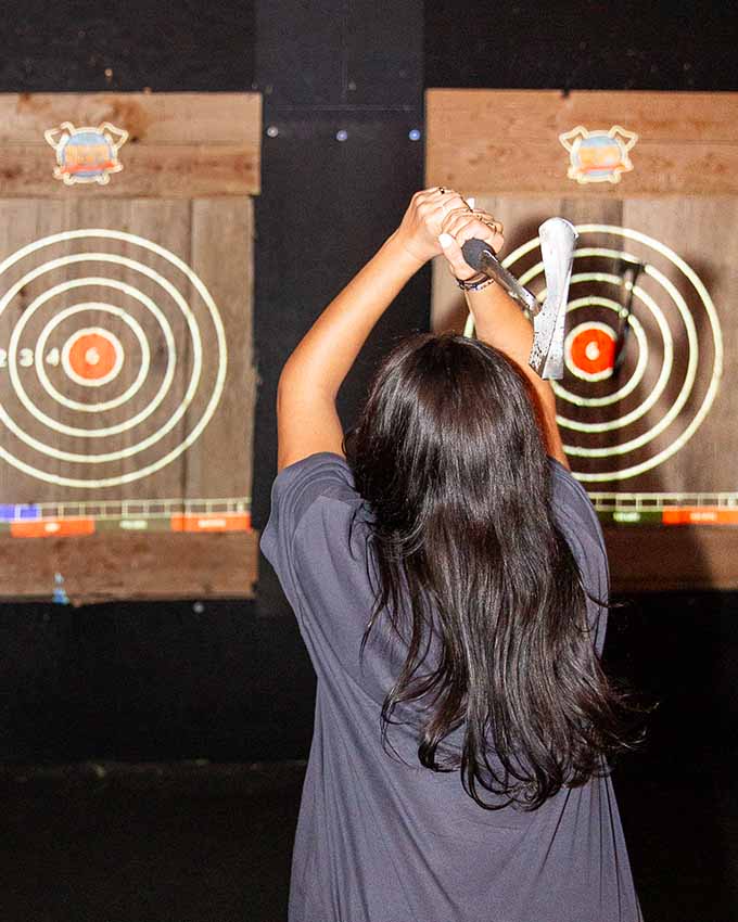 Woman with an axe overhead while preparing to throw at a wooden target.