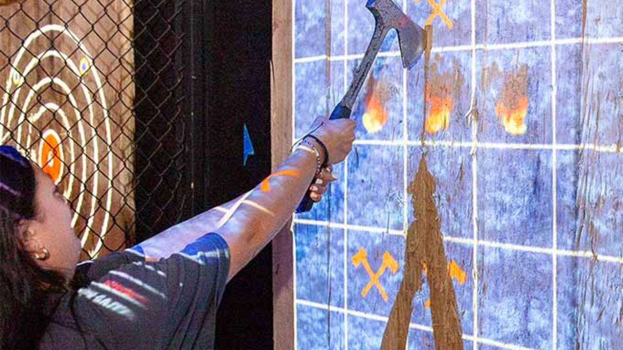 Woman practicing axe throwing at Montana Nights, aiming an axe at a wooden target board 