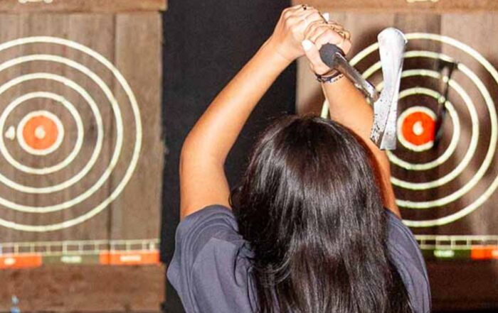 Woman aiming an axe at a projected target during an indoor axe throwing game.