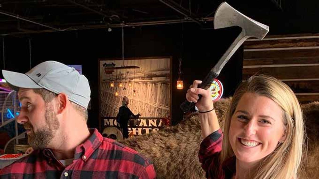 A couple posing indoors at an axe throwing venue, each holding an axe at Montana Nights 