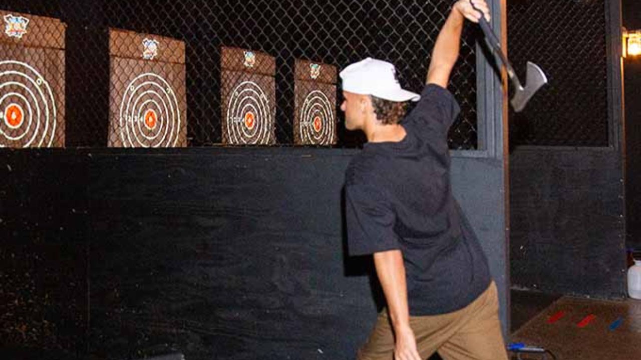 Person mid-throw stepping forward to release an axe toward wooden targets