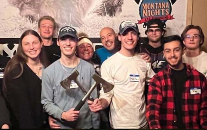 Smiling group of friends holding axes behind a wooden table at Montana Nights