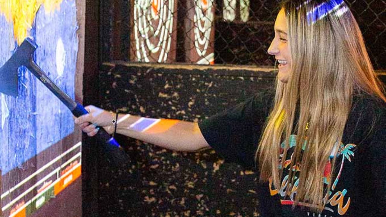 Woman smiling while throwing an axe at an interactive target at Montana Nights.
