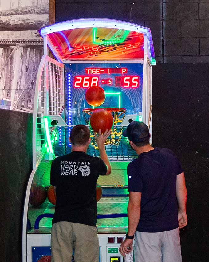 Two people playing arcade basketball with an illuminated scoreboard.
