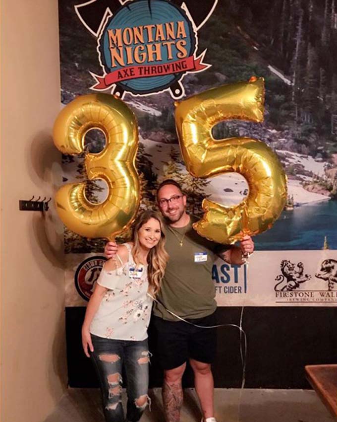 Couple holding large gold number balloons celebrating 35th birthday.