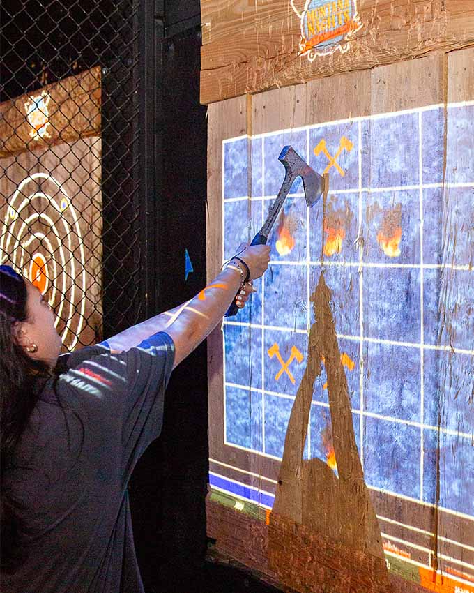 Participant playing an interactive digital axe throwing game on a projected target.