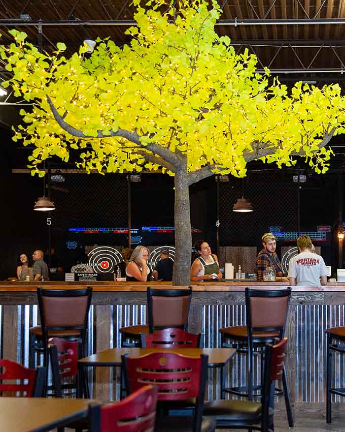 Rustic-themed axe throwing venue with seating areas, target lanes, and decorative indoor landscaping for guests
