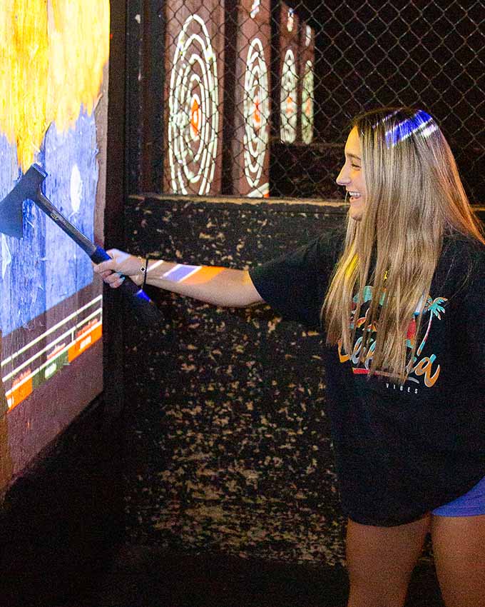 Smiling guest using an axe to interact with a projected digital target game inside Montana Nights