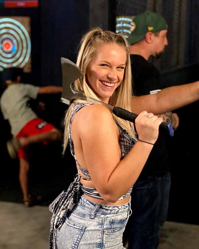 Smiling participant holding an axe while enjoying a fun social activity.