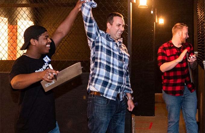 Winner celebrating after an axe throwing competition with friends cheering inside the venue.