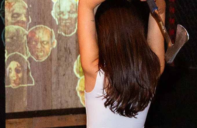 Woman preparing to throw an axe at a digital zombie-themed target during an interactive axe throwing game indoors