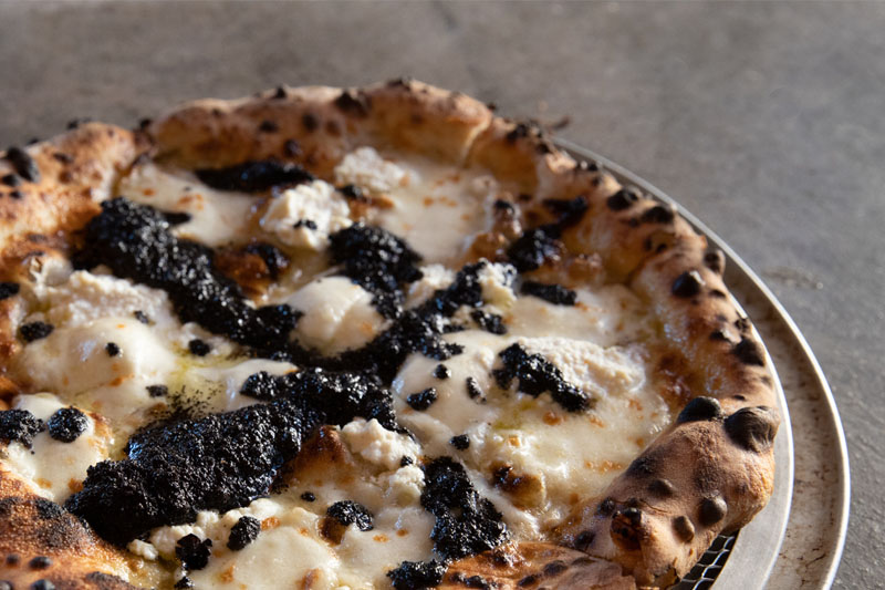 Gourmet wood-fired pizza topped with creamy cheese, ricotta, and black truffle for a premium dining experience.