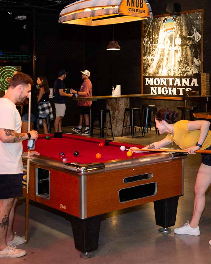 Guests enjoying pool and arcade games at Montana Nights entertainment venue before an axe throwing session.