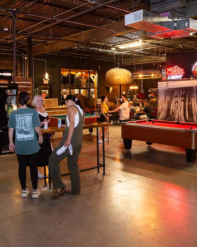 Guests socializing around pool tables and arcade games at Montana Nights.