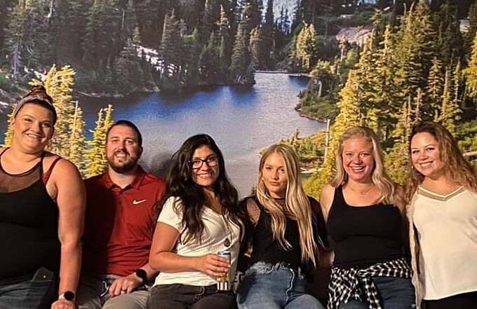 Friends posing together in front of a scenic mountain lake background.