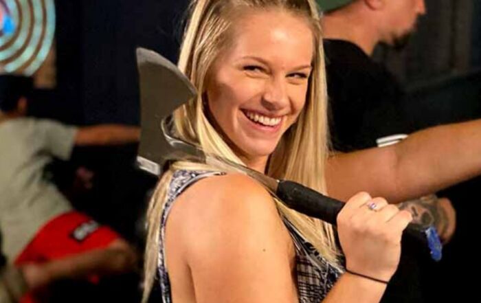 Smiling woman holding an axe at Montana Nights axe-throwing venue.