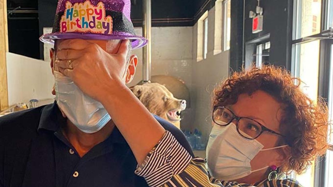 Woman adjusting a purple birthday hat on a man during an indoor birthday celebration.